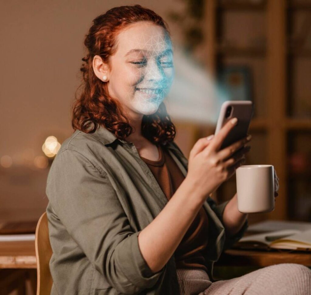 A woman smiling at her smartphone, holding a coffee mug, with a facial recognition overlay on her face.