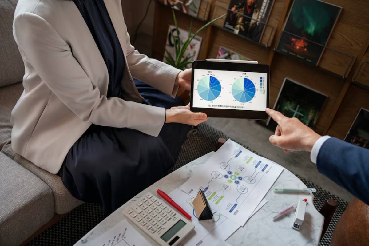 Two business professionals reviewing pie charts on a tablet during a meeting, with documents and a calculator on the table.