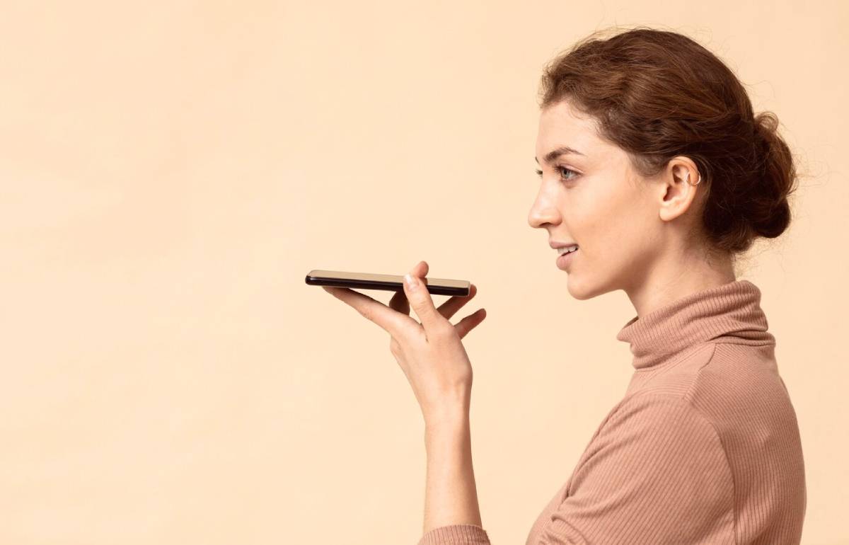  Woman using voice commands on her smartphone against a beige background.