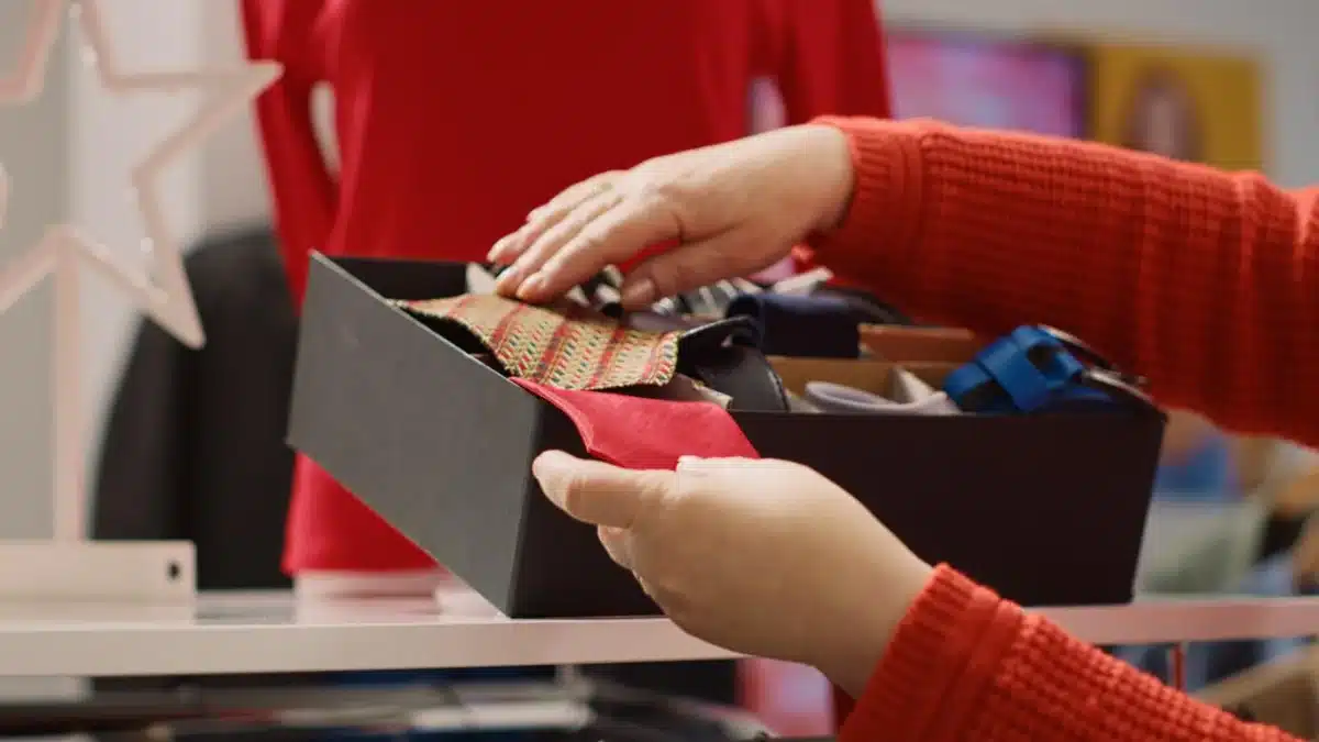 Hands packing a colourful scarf into a gift box in a festive setting.