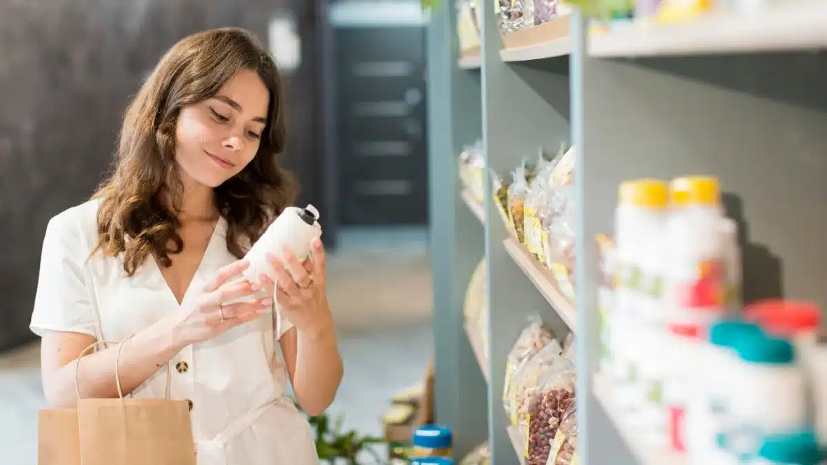 Woman examines a product in a grocery store with shelves of food items in the background.