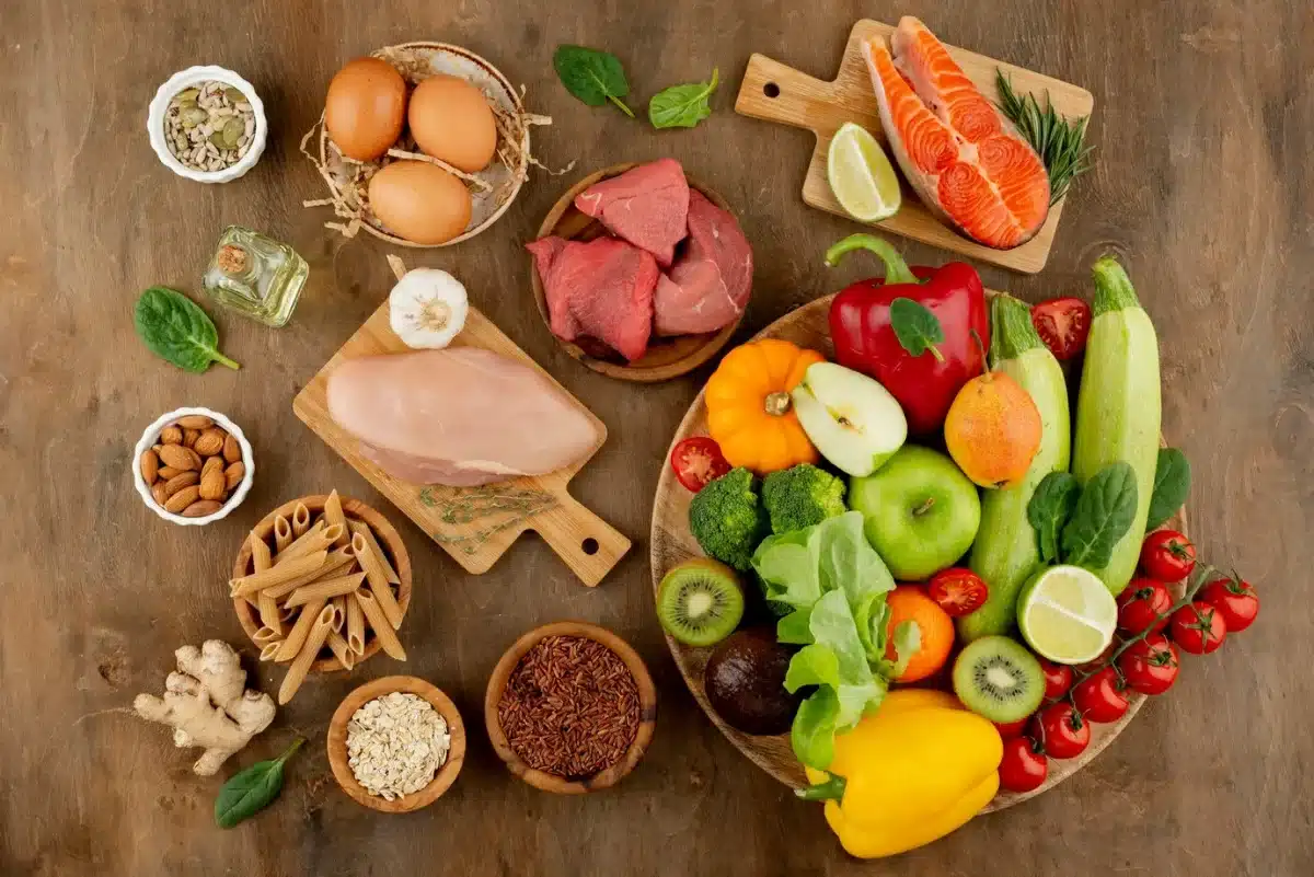 Assorted healthy foods including fruits, vegetables, meats, eggs, and nuts on a wooden surface.